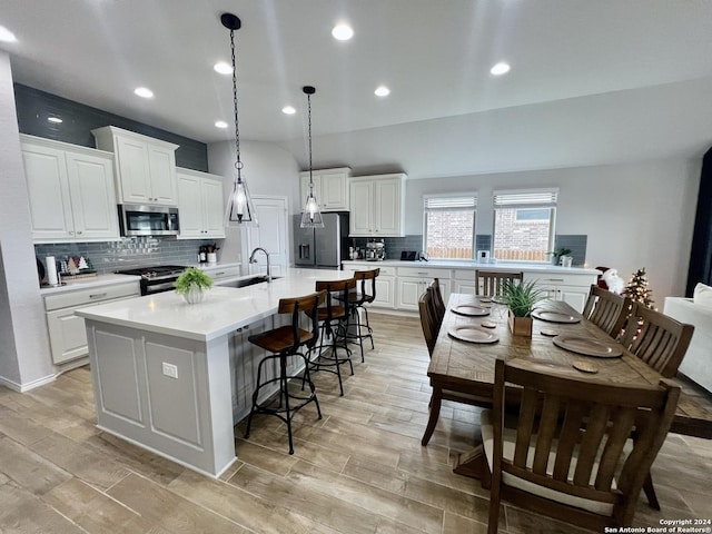 kitchen with decorative backsplash, appliances with stainless steel finishes, a large island with sink, pendant lighting, and white cabinets