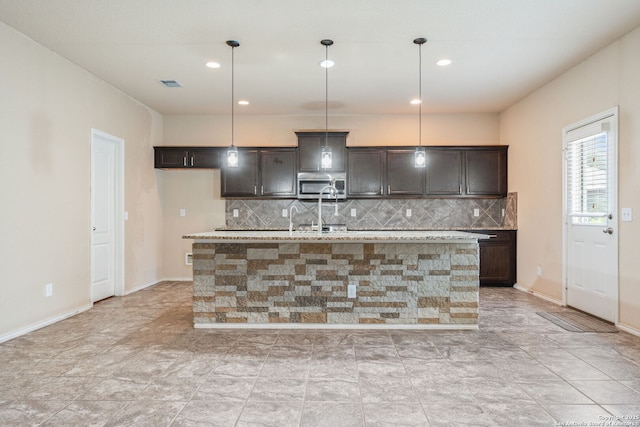 kitchen featuring tasteful backsplash, dark brown cabinetry, an island with sink, and hanging light fixtures