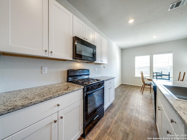 kitchen featuring black appliances, light hardwood / wood-style floors, a textured ceiling, light stone counters, and white cabinets