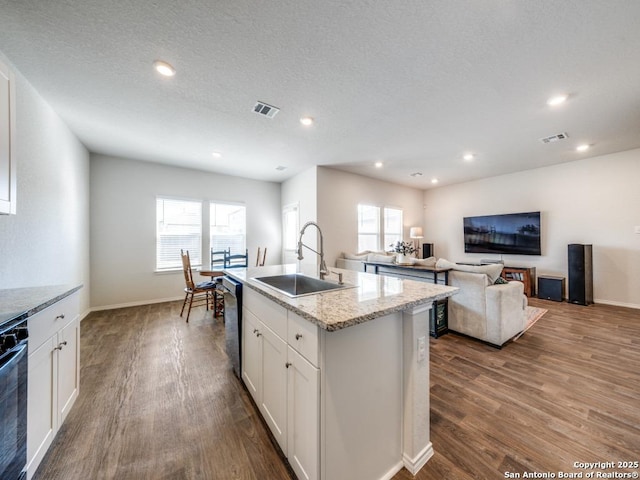 kitchen with sink, white cabinetry, hardwood / wood-style floors, stainless steel dishwasher, and a kitchen island with sink