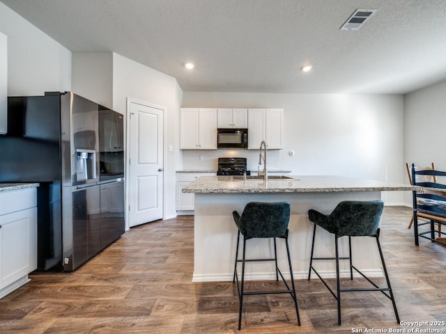 kitchen featuring sink, white cabinetry, stove, stainless steel fridge, and a kitchen island with sink