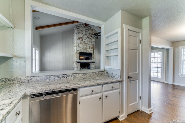 kitchen with stainless steel dishwasher, white cabinets, beamed ceiling, and a stone fireplace