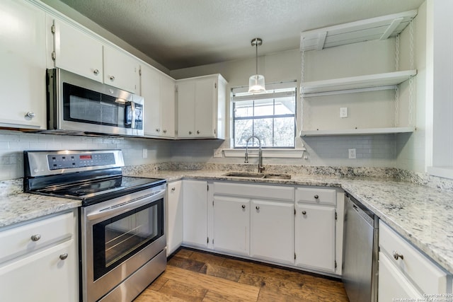 kitchen with sink, decorative light fixtures, white cabinets, light stone countertops, and appliances with stainless steel finishes