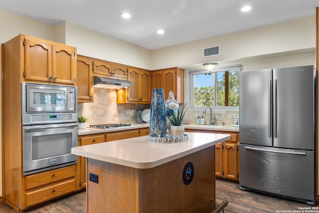 kitchen featuring appliances with stainless steel finishes, sink, backsplash, dark hardwood / wood-style flooring, and a center island