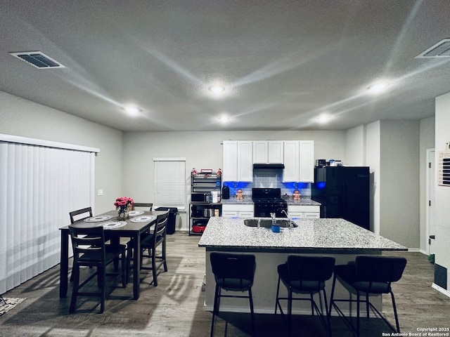 kitchen with decorative backsplash, light stone counters, black appliances, a center island with sink, and white cabinetry