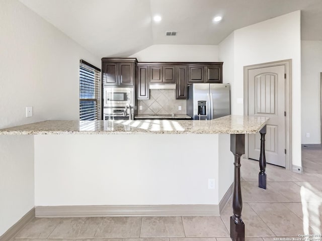 kitchen with stainless steel appliances, vaulted ceiling, light stone counters, a kitchen breakfast bar, and backsplash