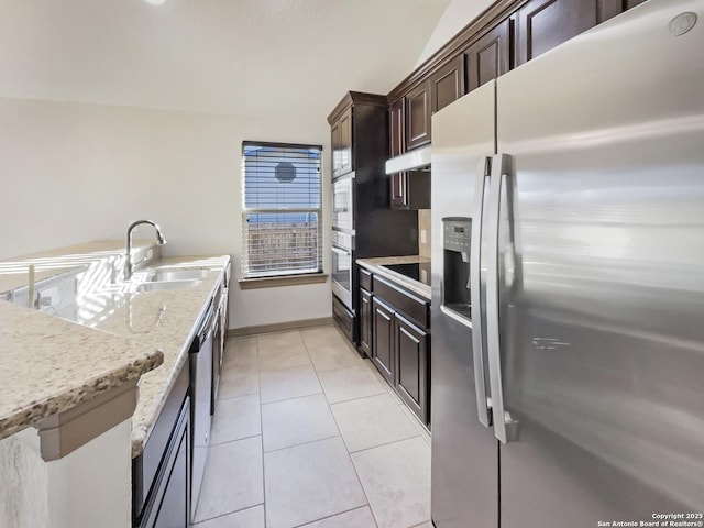 kitchen with appliances with stainless steel finishes, light stone countertops, light tile patterned floors, sink, and dark brown cabinets