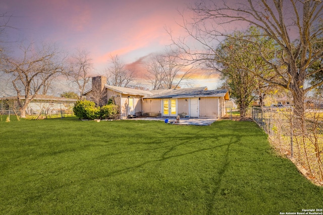 back house at dusk featuring a yard and a patio