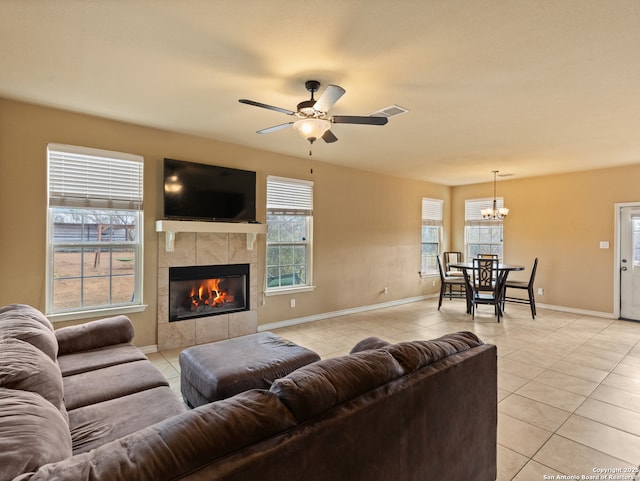 tiled living room with a tiled fireplace and ceiling fan with notable chandelier