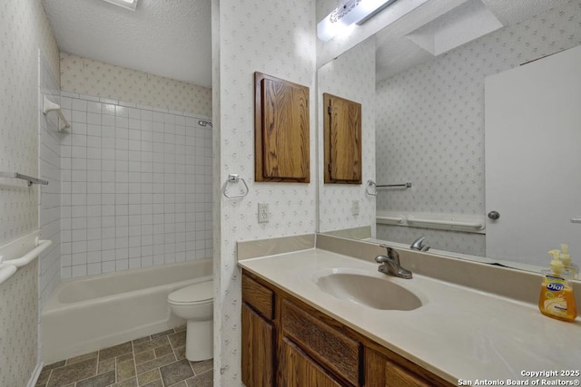 full bathroom featuring a textured ceiling, vanity, tiled shower / bath combo, and toilet