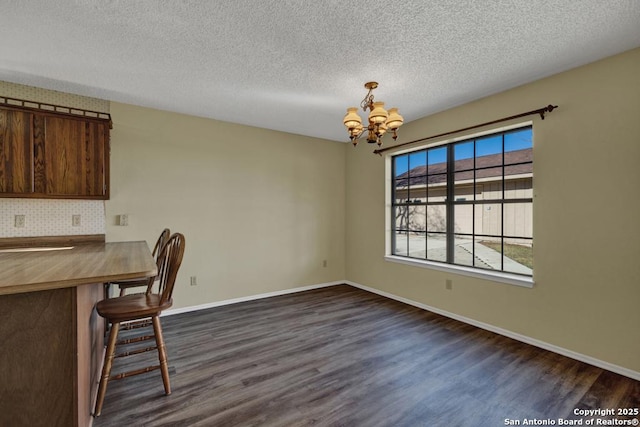 unfurnished dining area with dark wood-type flooring, a textured ceiling, and a chandelier