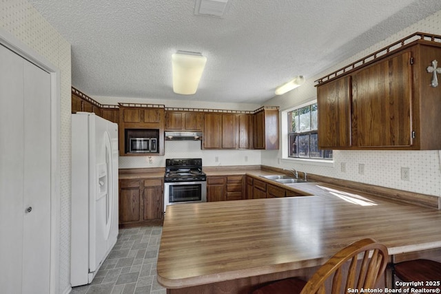 kitchen with sink, a textured ceiling, kitchen peninsula, and appliances with stainless steel finishes