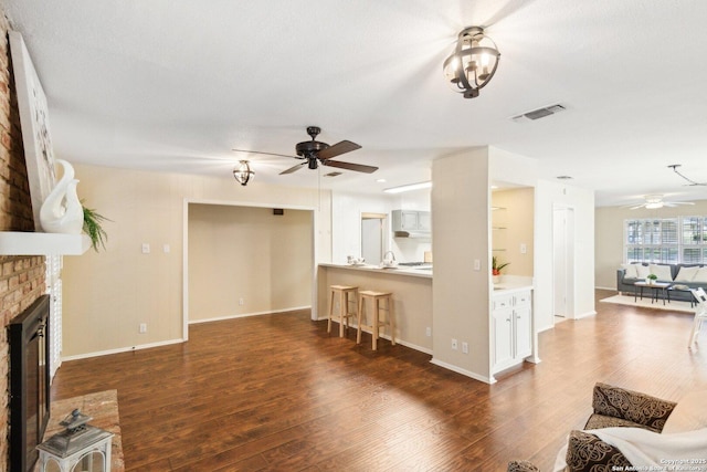 living room featuring dark hardwood / wood-style flooring, a brick fireplace, and ceiling fan