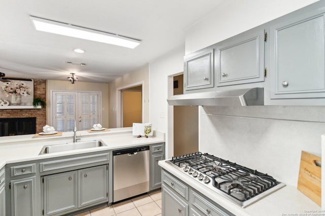 kitchen with light tile patterned floors, gray cabinets, a fireplace, appliances with stainless steel finishes, and sink