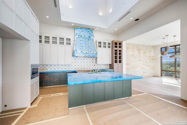 kitchen featuring a kitchen island with sink, sink, white cabinets, and decorative light fixtures