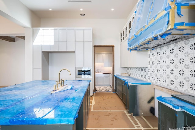 kitchen featuring sink, backsplash, stainless steel microwave, white cabinets, and light tile patterned flooring