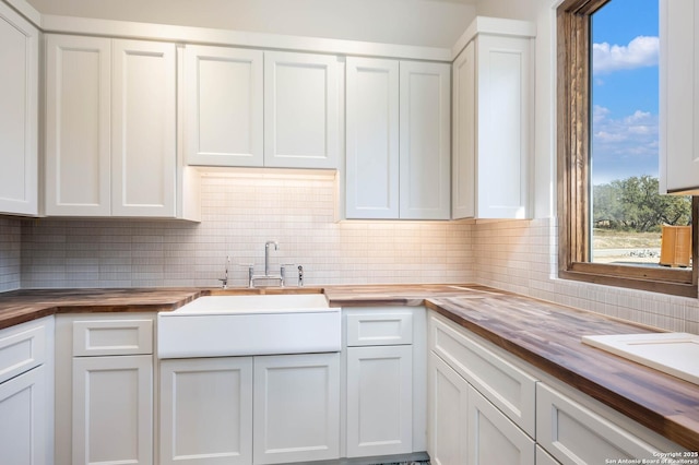 kitchen with white cabinetry, butcher block counters, sink, and backsplash