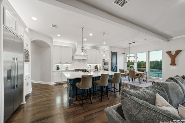 kitchen featuring a barn door, appliances with stainless steel finishes, pendant lighting, beam ceiling, and white cabinetry