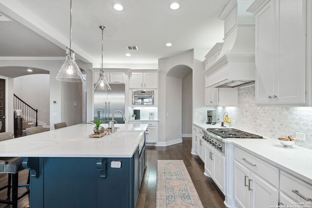 kitchen with stainless steel appliances, a center island with sink, white cabinets, and decorative light fixtures