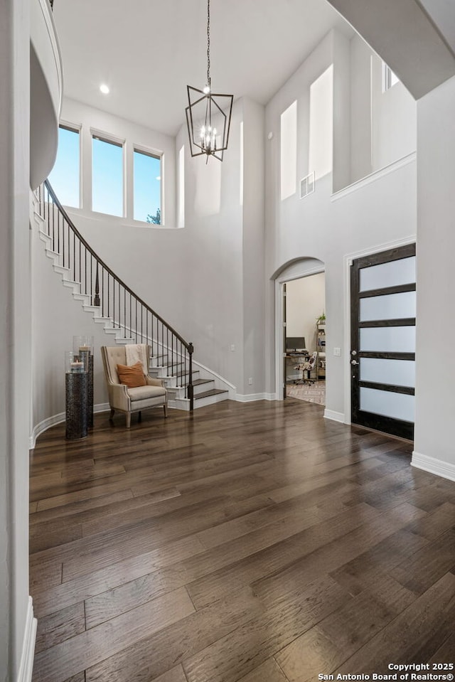 entrance foyer with dark wood-type flooring, a towering ceiling, and a chandelier