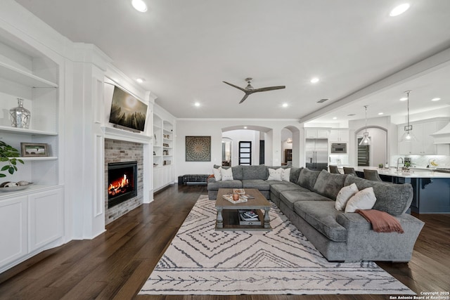 living room featuring sink, a fireplace, ceiling fan, built in features, and dark hardwood / wood-style flooring