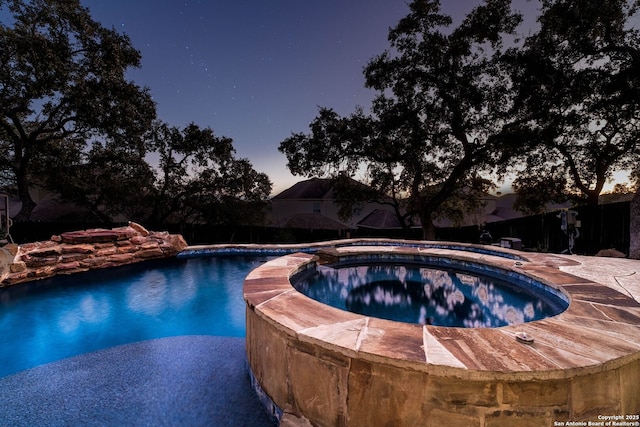 pool at dusk featuring an in ground hot tub