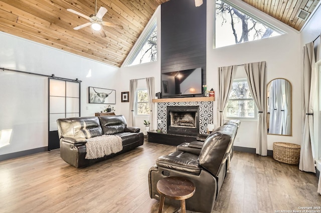 living room with light hardwood / wood-style flooring, a tile fireplace, high vaulted ceiling, a barn door, and wooden ceiling