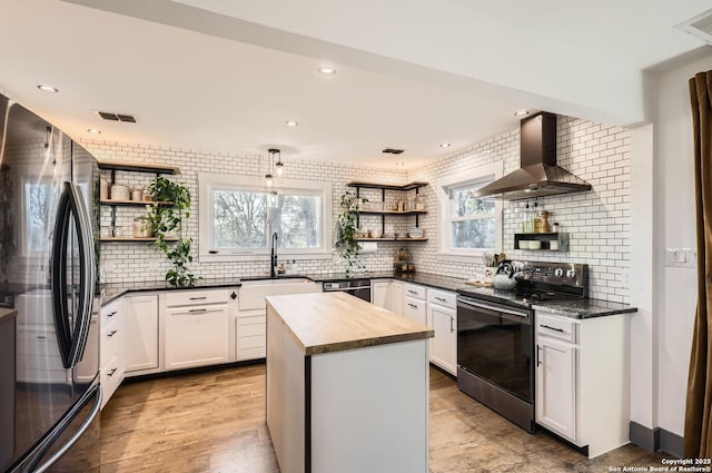 kitchen with a center island, stainless steel appliances, wall chimney range hood, white cabinetry, and sink