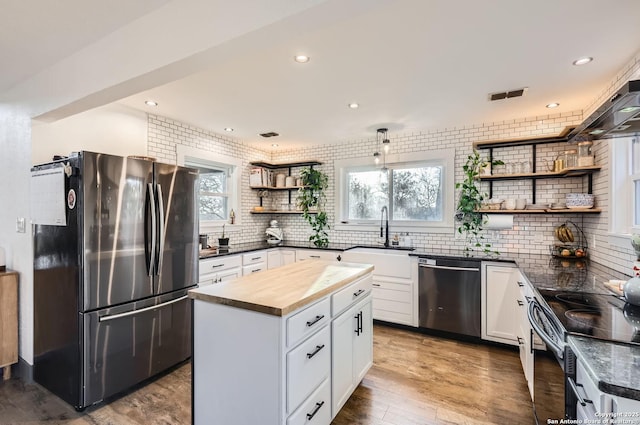 kitchen with stainless steel appliances, sink, white cabinets, a center island, and wooden counters