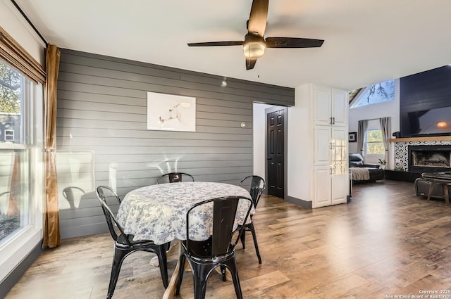 dining room with a tile fireplace, ceiling fan, wooden walls, and light hardwood / wood-style flooring