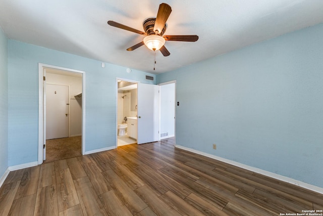 unfurnished bedroom featuring ceiling fan, a walk in closet, connected bathroom, and hardwood / wood-style flooring