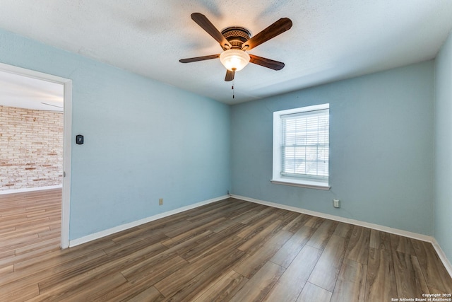 unfurnished room with dark wood-type flooring, brick wall, ceiling fan, and a textured ceiling