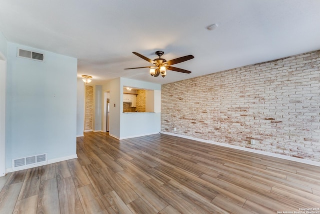 empty room featuring ceiling fan, light wood-type flooring, and brick wall