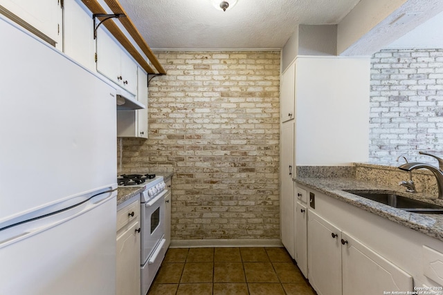 kitchen featuring sink, white cabinets, a textured ceiling, white appliances, and brick wall