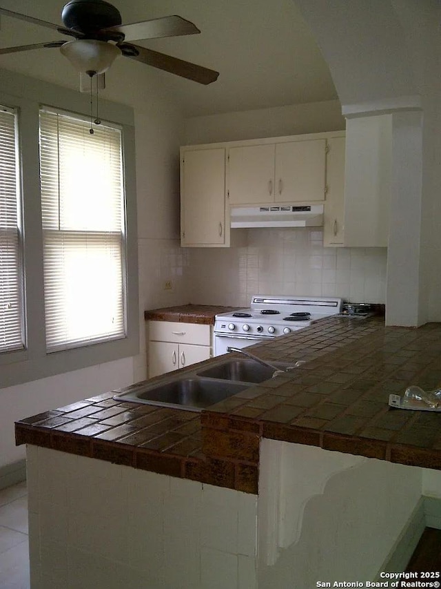 kitchen with white electric range oven, tile countertops, backsplash, and white cabinetry