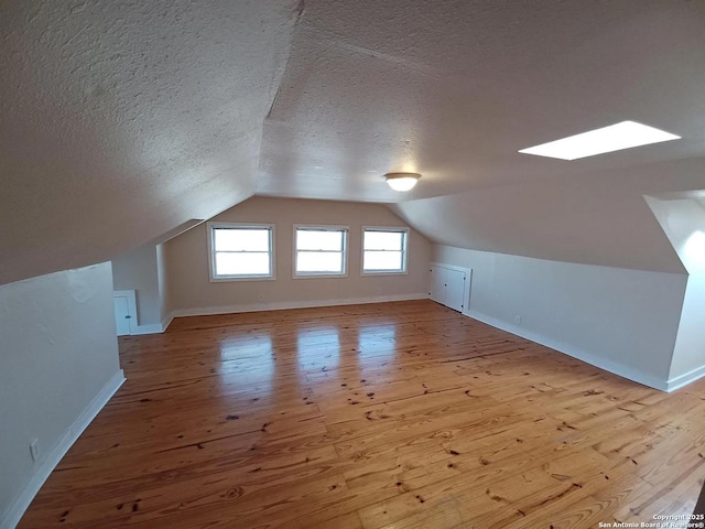 bonus room with lofted ceiling with skylight, a textured ceiling, and light hardwood / wood-style floors