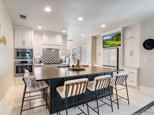 kitchen featuring stainless steel appliances, an island with sink, a kitchen breakfast bar, and white cabinetry