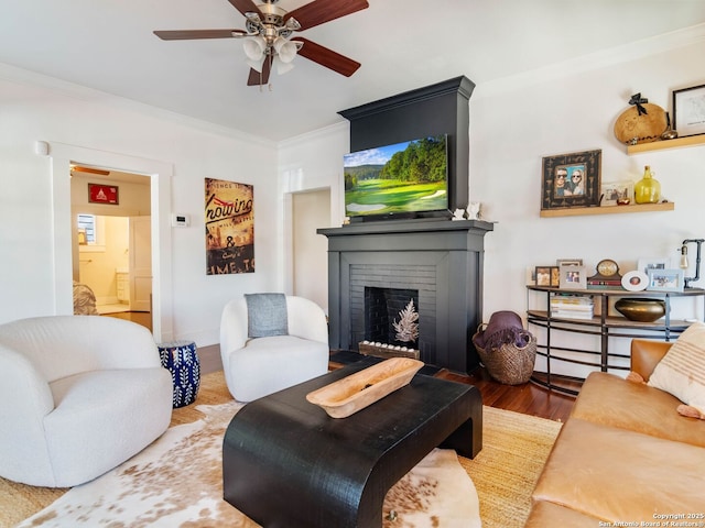 living room featuring ornamental molding, a brick fireplace, wood-type flooring, and ceiling fan