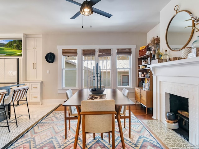 dining area with a brick fireplace, ceiling fan, and light hardwood / wood-style flooring