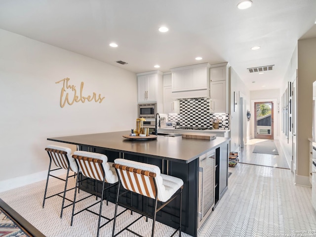 kitchen featuring a breakfast bar area, stainless steel appliances, white cabinets, and a center island with sink