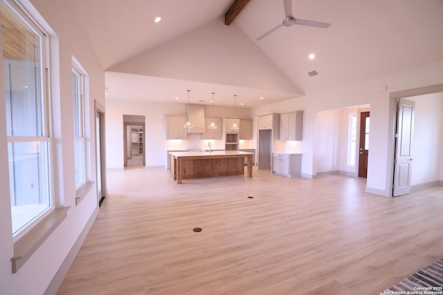 unfurnished living room featuring light wood-type flooring, ceiling fan, high vaulted ceiling, a wealth of natural light, and beam ceiling