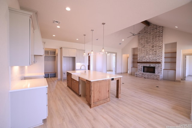 kitchen featuring decorative light fixtures, a large island, a brick fireplace, white cabinetry, and ceiling fan