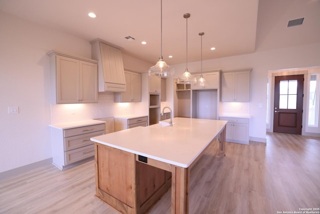 kitchen featuring pendant lighting, an island with sink, light hardwood / wood-style floors, decorative backsplash, and sink