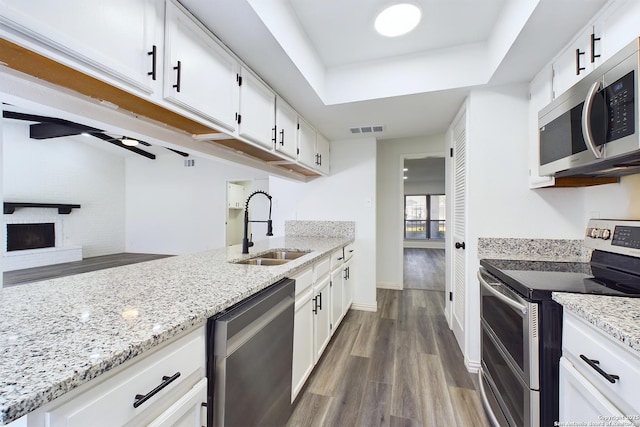 kitchen with dark wood-type flooring, white cabinets, appliances with stainless steel finishes, a fireplace, and sink