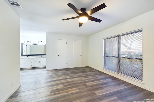 unfurnished bedroom featuring ensuite bath, multiple closets, ceiling fan, and dark hardwood / wood-style floors