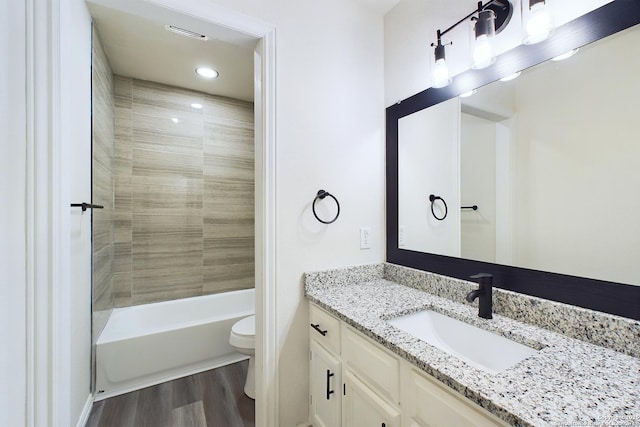 full bathroom featuring wood-type flooring, tiled shower / bath, vanity, and toilet