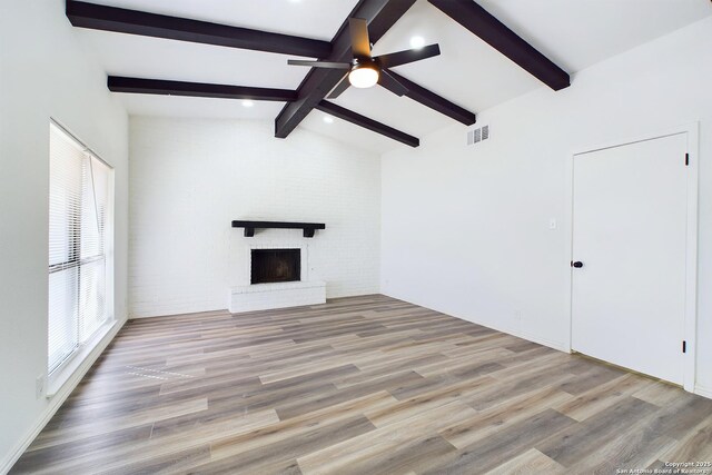 unfurnished living room with lofted ceiling with beams, brick wall, ceiling fan, a brick fireplace, and light hardwood / wood-style flooring