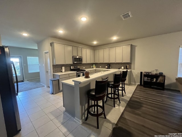 kitchen featuring a kitchen breakfast bar, light tile patterned floors, decorative backsplash, a kitchen island, and appliances with stainless steel finishes