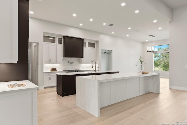 kitchen featuring white cabinetry, ceiling fan, a kitchen island with sink, light wood-type flooring, and sink