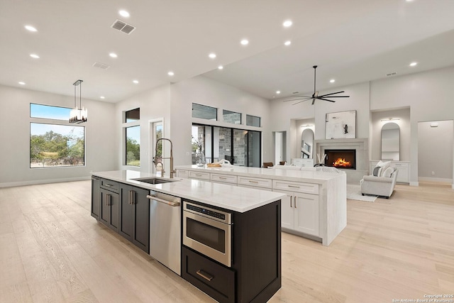 kitchen with decorative light fixtures, a center island with sink, sink, white cabinetry, and stainless steel appliances